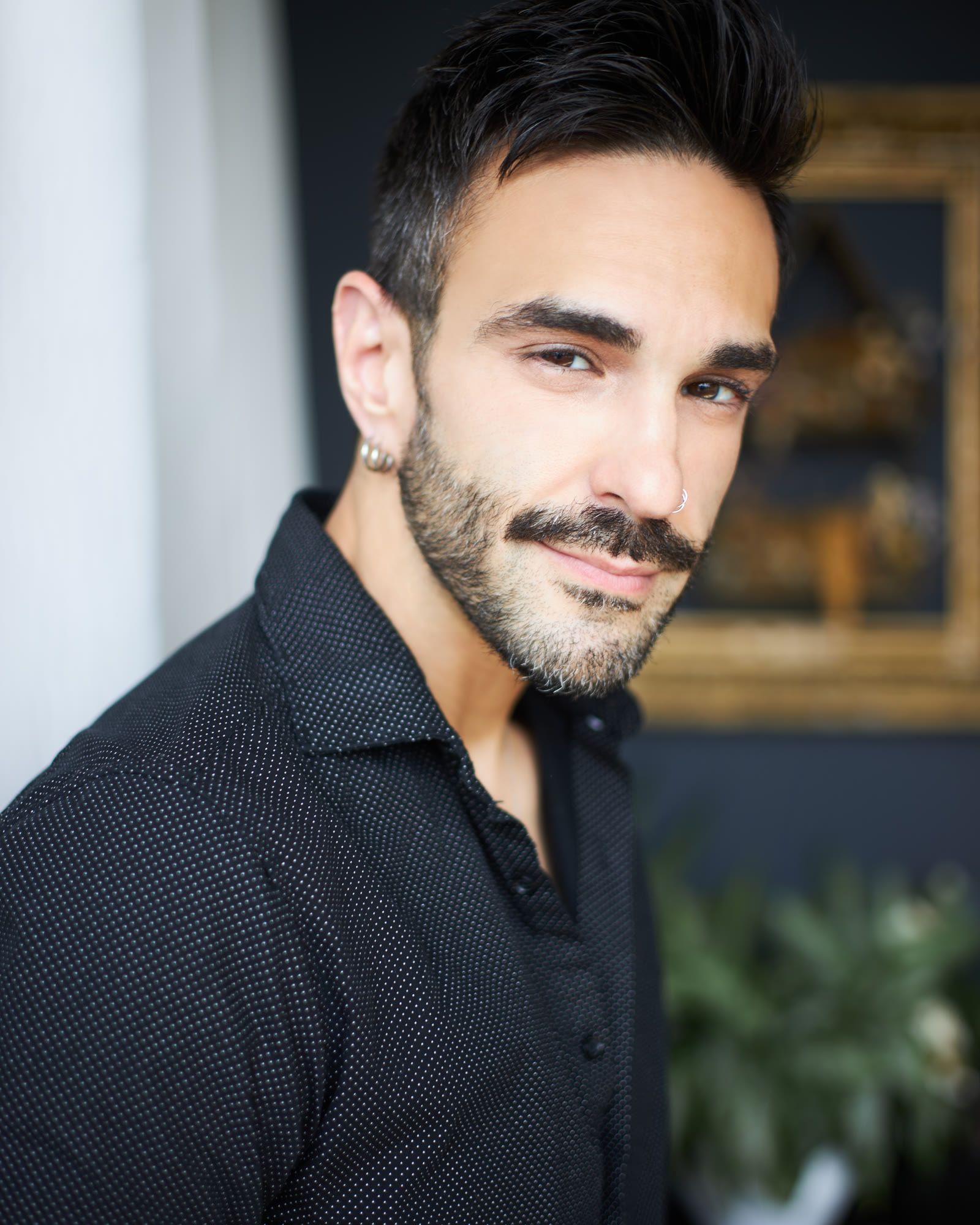 Peter Andrew Danzig in a dark collared shirt, close portrait, looking at the camera with a relaxed smile, with greenery blurred behind.